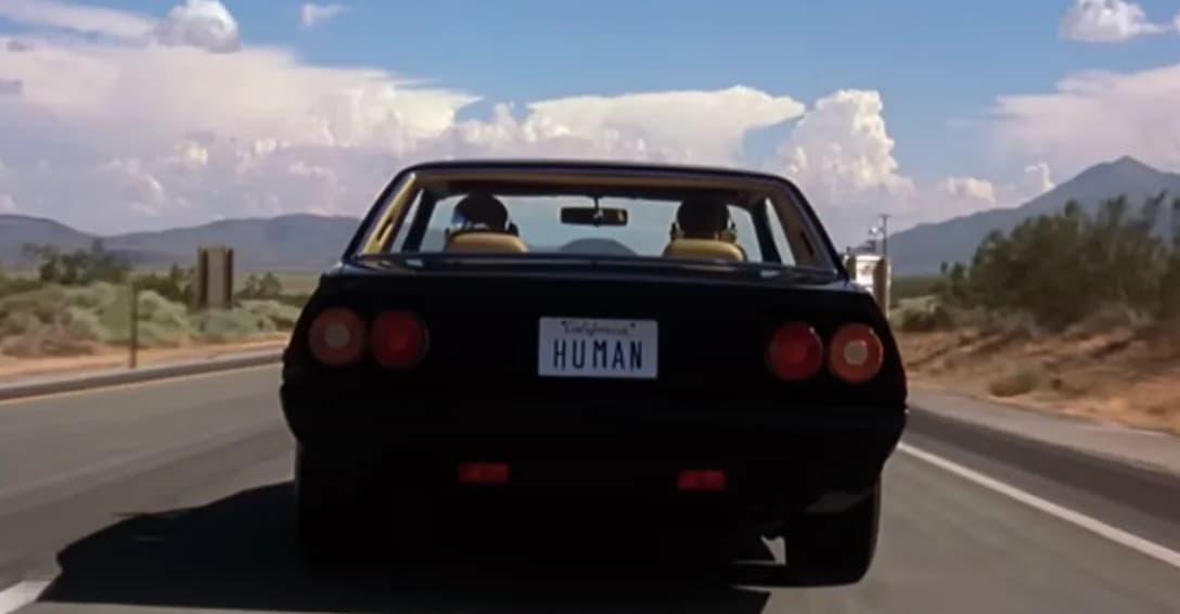 A black car with a HUMAN license plate driving through a southwestern desert landscape
