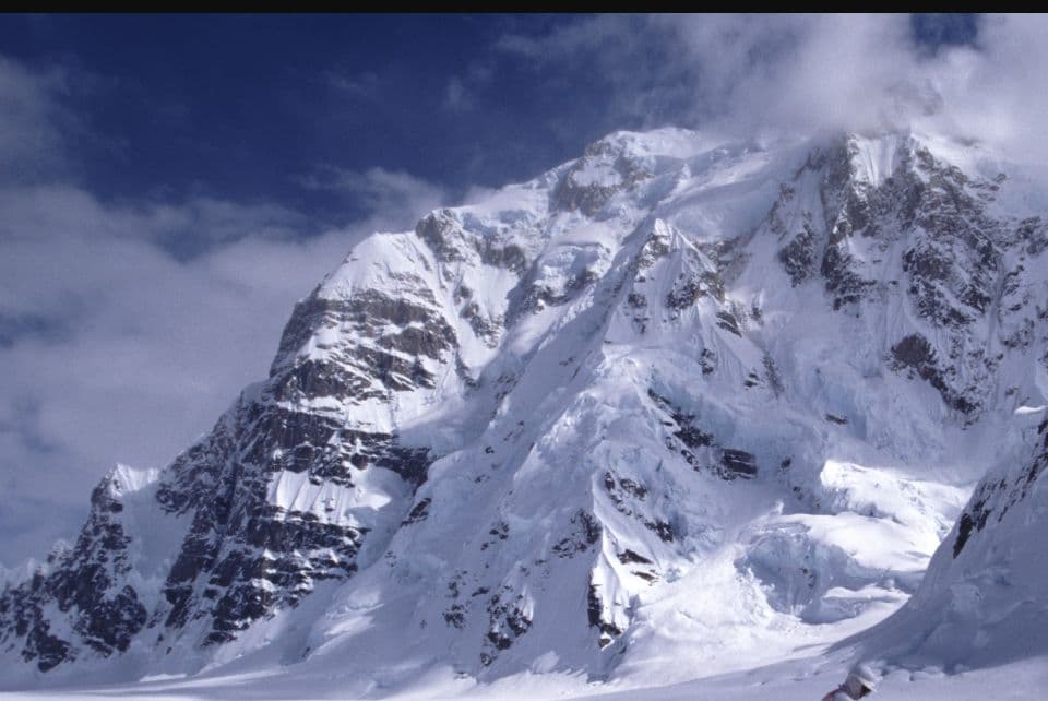 Editorial illustration of two small alpine climbers moving across a vast, steep ice-and-rock mountain face
